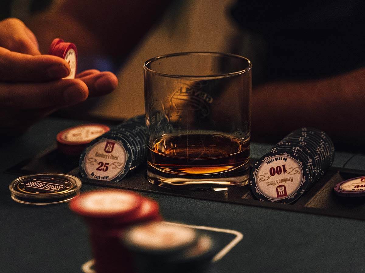A poker player flipping his chips in his fingers while sitting at a table with a whiskey drink.